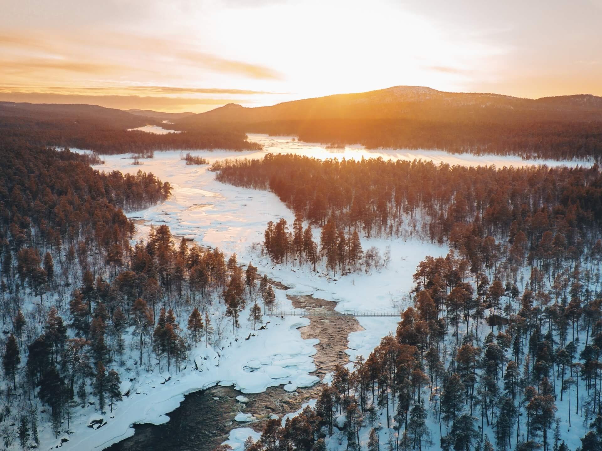 Een besneeuwde rivier en bossen in het warme winterlicht van Lapland